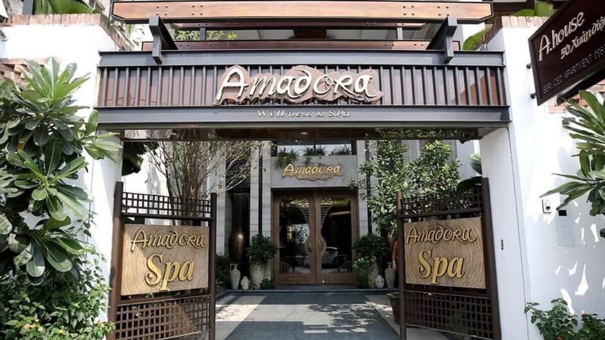 The entrance of Amadora Wellness & Spa in Hanoi, featuring elegant wooden signage, lush greenery, and a welcoming facade in the city's Old Quarter.