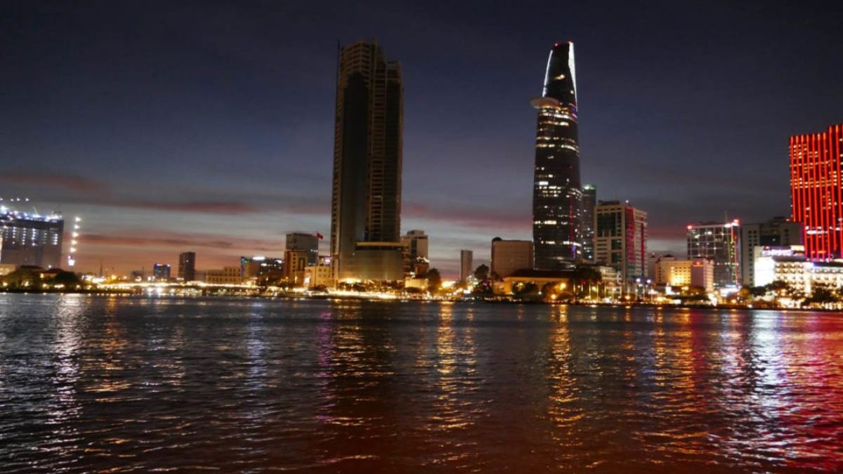 Bitexco Financial Tower rises above the Ho Chi Minh City skyline at dusk, with its illuminated façade reflecting on the Saigon River and surrounding skyscrapers.
