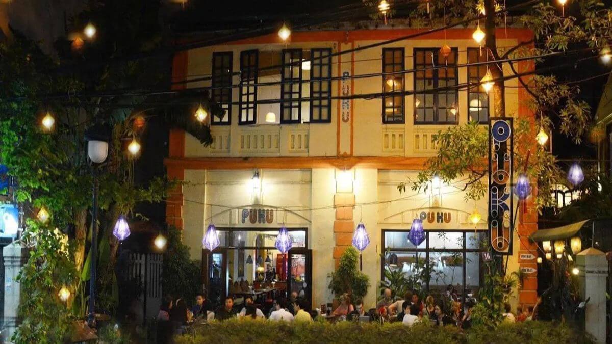 Outdoor café at night in Vietnam with warm hanging lights, guests enjoying drinks, and a cozy colonial-style building creating a charming evening atmosphere.