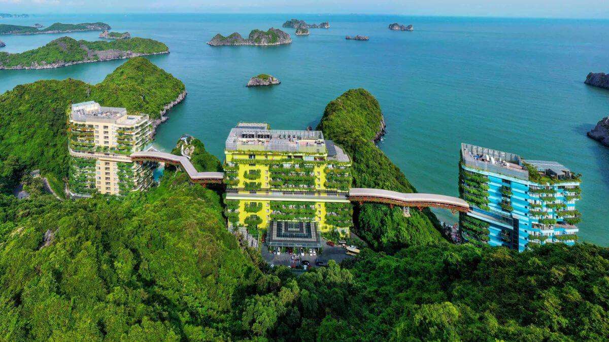 Aerial view of Flamingo Cat Ba Resort with green architecture buildings and overhead walkways overlooking the bay.