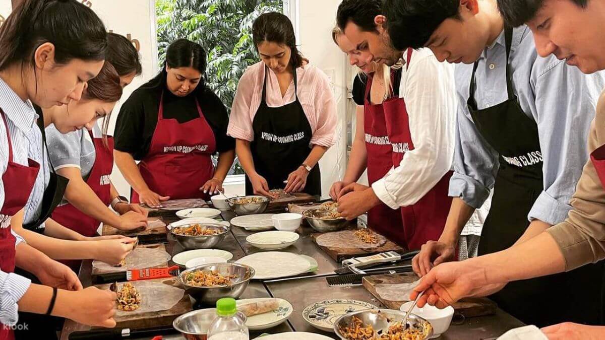 A group of international visitors wearing aprons prepares traditional Vietnamese dishes together during a hands-on cooking class in Hanoi.
