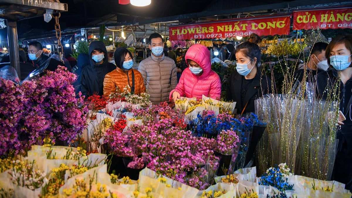 Visitors browse vibrant bouquets and fresh flowers at Ho Thi Ky Flower Market, the largest wholesale flower market in Ho Chi Minh City, illuminated by colorful lights at night.