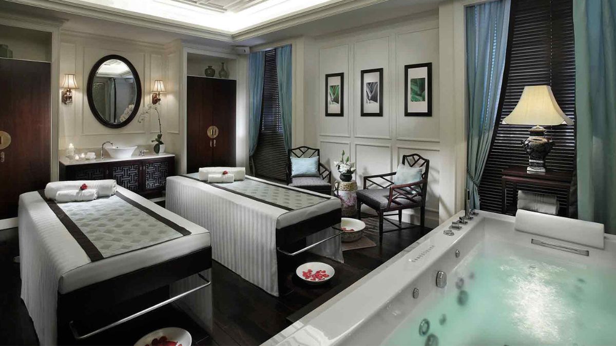 A luxurious spa treatment room in Hanoi featuring two massage beds, a whirlpool bathtub, elegant décor, soft lighting, and a peaceful atmosphere designed for couples' wellness experiences.
