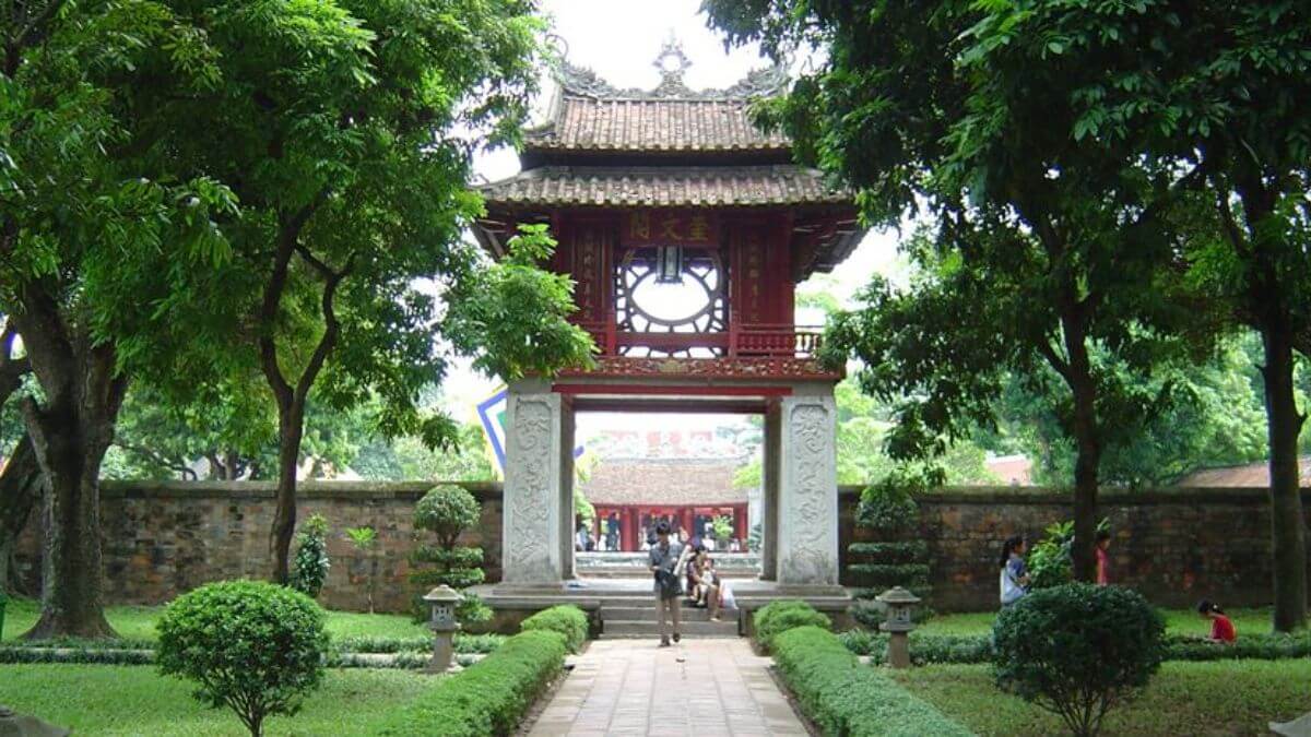 The entrance gate of the Temple of Literature in Hanoi, Vietnam, surrounded by lush green trees and neatly landscaped gardens, welcomes visitors to the country's first national university.