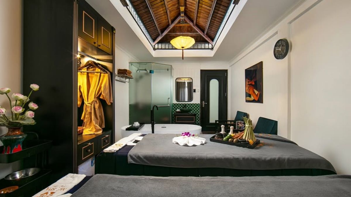 A private spa treatment room in Hanoi featuring two massage beds, a freestanding bathtub, elegant wooden ceiling beams, and a relaxing, modern interior.