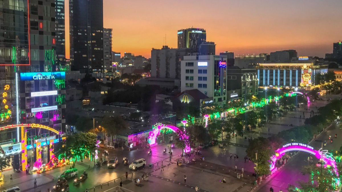 A panoramic evening view of Nguyen Hue Walking Street in Ho Chi Minh City, illuminated with colorful lights, modern skyscrapers, and bustling crowds enjoying the vibrant city atmosphere.