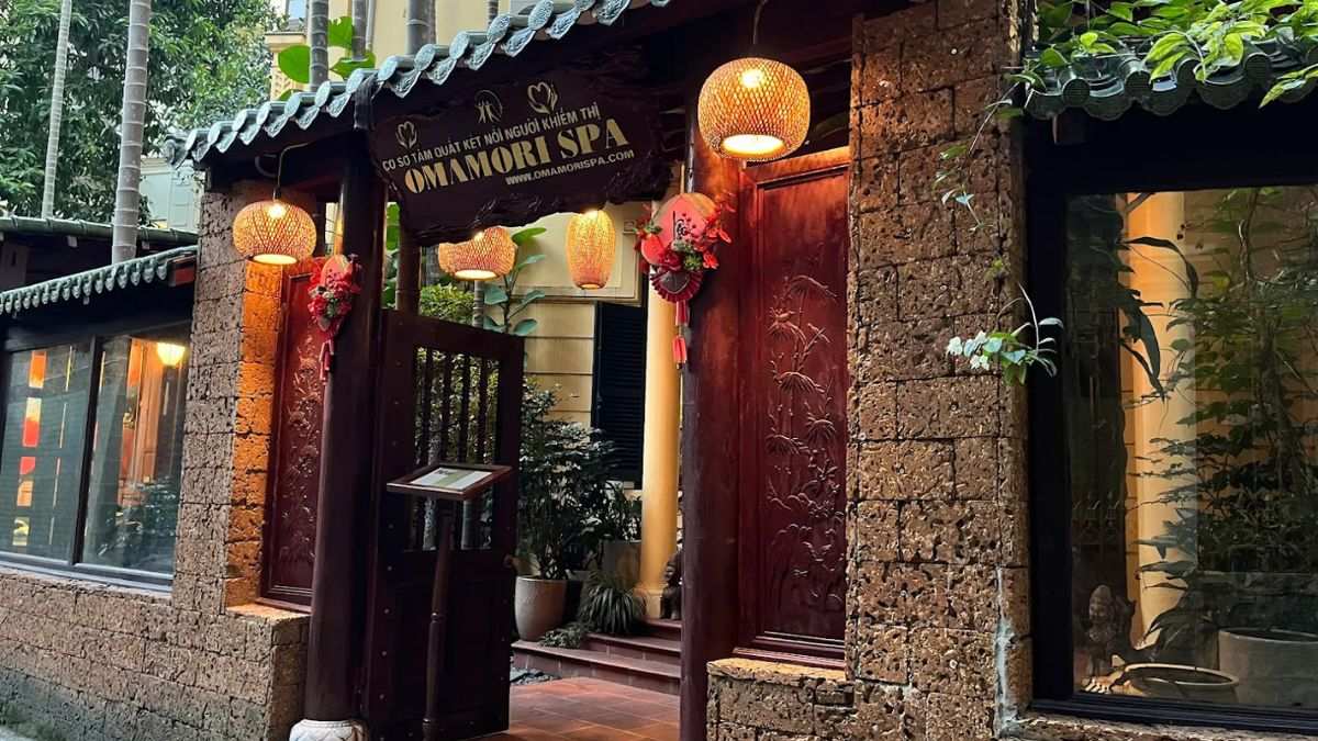 Traditional-style entrance to Omamori Spa in Hanoi, featuring rustic stone walls, wooden gates, warm lanterns, and lush greenery that create a peaceful and welcoming atmosphere.