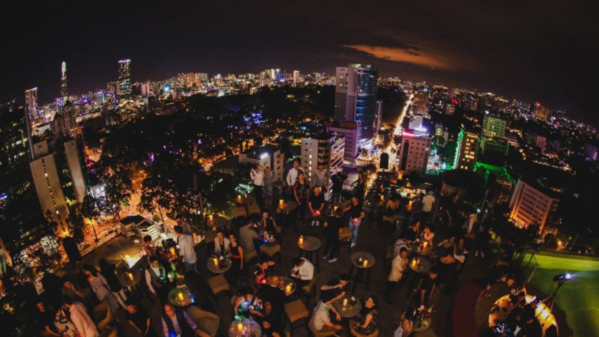 A lively rooftop bar in Ho Chi Minh City overlooking the illuminated skyline at night, where guests enjoy drinks and panoramic views of the city's vibrant nightlife.