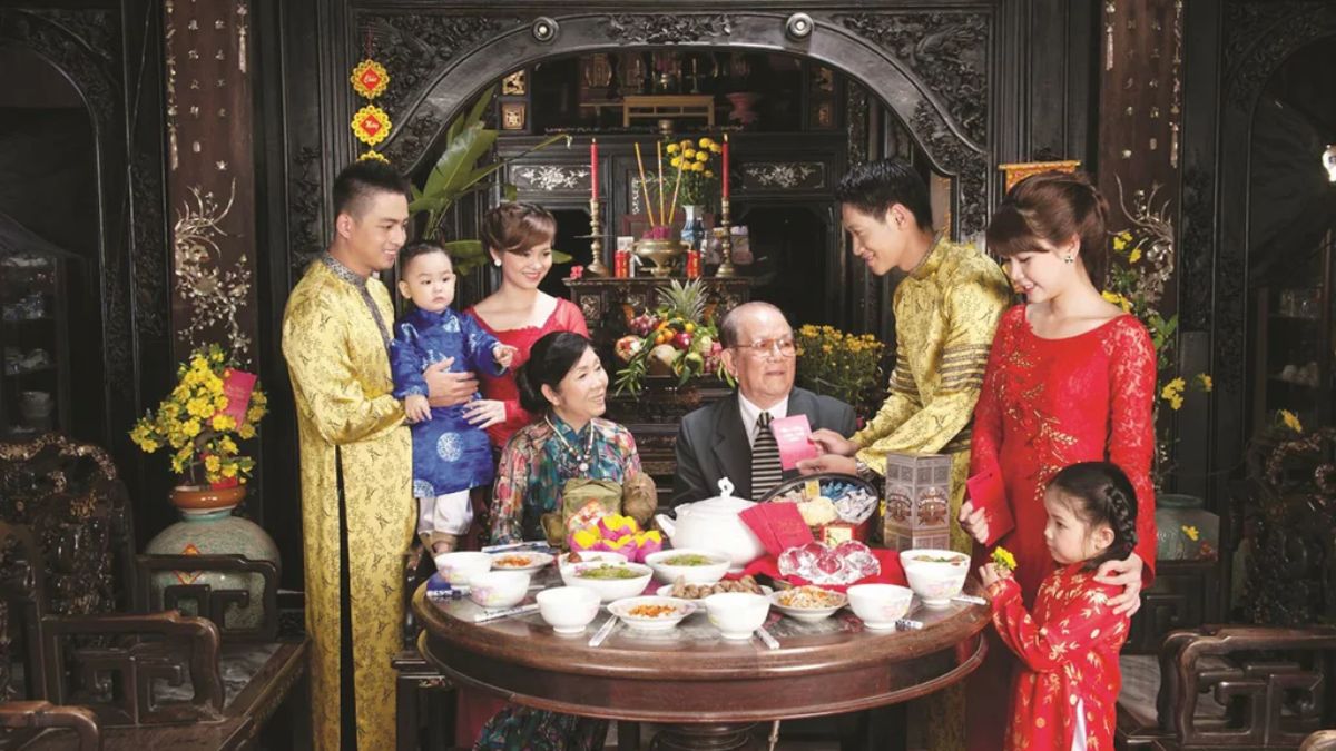 A Vietnamese family wearing traditional áo dài gathers around a festive table during Tết, as younger family members present lucky money to their grandparents in a beautifully decorated ancestral home.