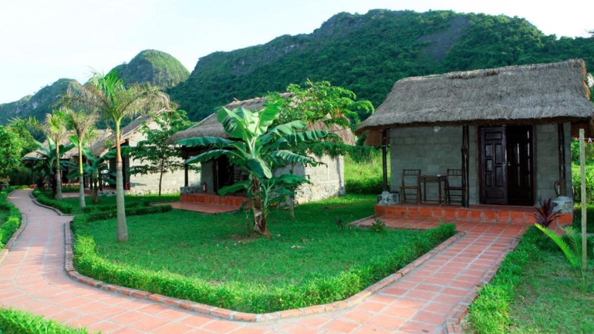 Traditional thatched-roof bungalows at Whisper Nature Bungalow in Cat Ba, surrounded by lush green lawns and limestone mountains.