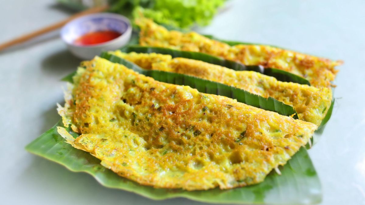 A golden Vietnamese bánh xèo filled with shrimp, pork, and bean sprouts, served with fresh herbs, lettuce, and a traditional dipping sauce.