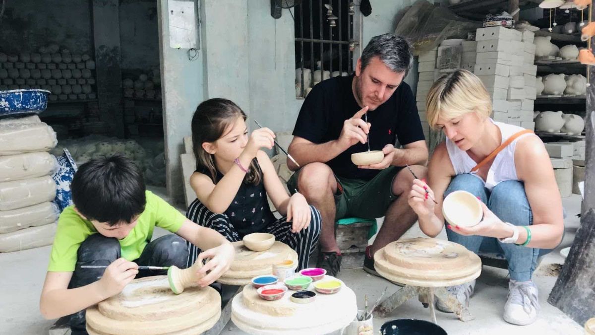 An international family and their children paint ceramic items at Bat Trang Ceramic Village, participating in a hands-on pottery workshop with local artisans.
