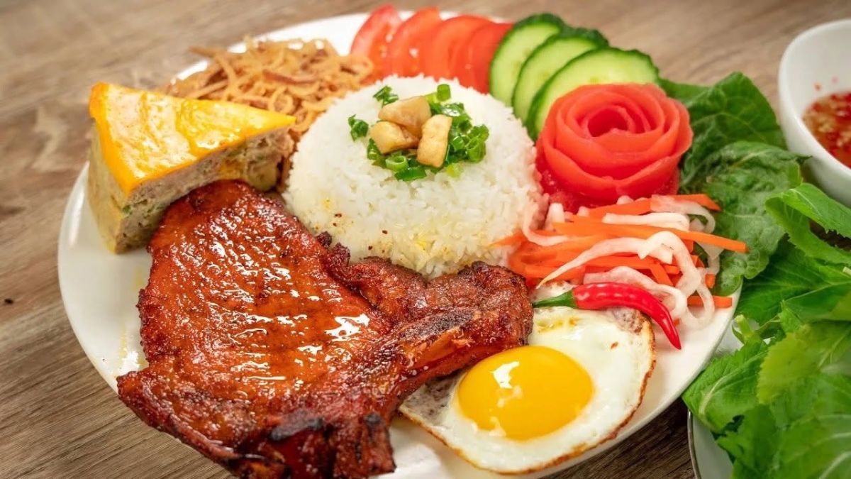 A plate of Vietnamese broken rice (Cơm Tấm) served with grilled pork, a fried egg, pickled vegetables, and fish sauce, showcasing one of Vietnam’s most beloved comfort foods.