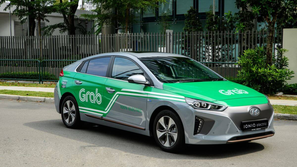 A green and silver Grab taxi parked on a city street in Vietnam, featuring the Grab logo and modern ride-hailing branding.