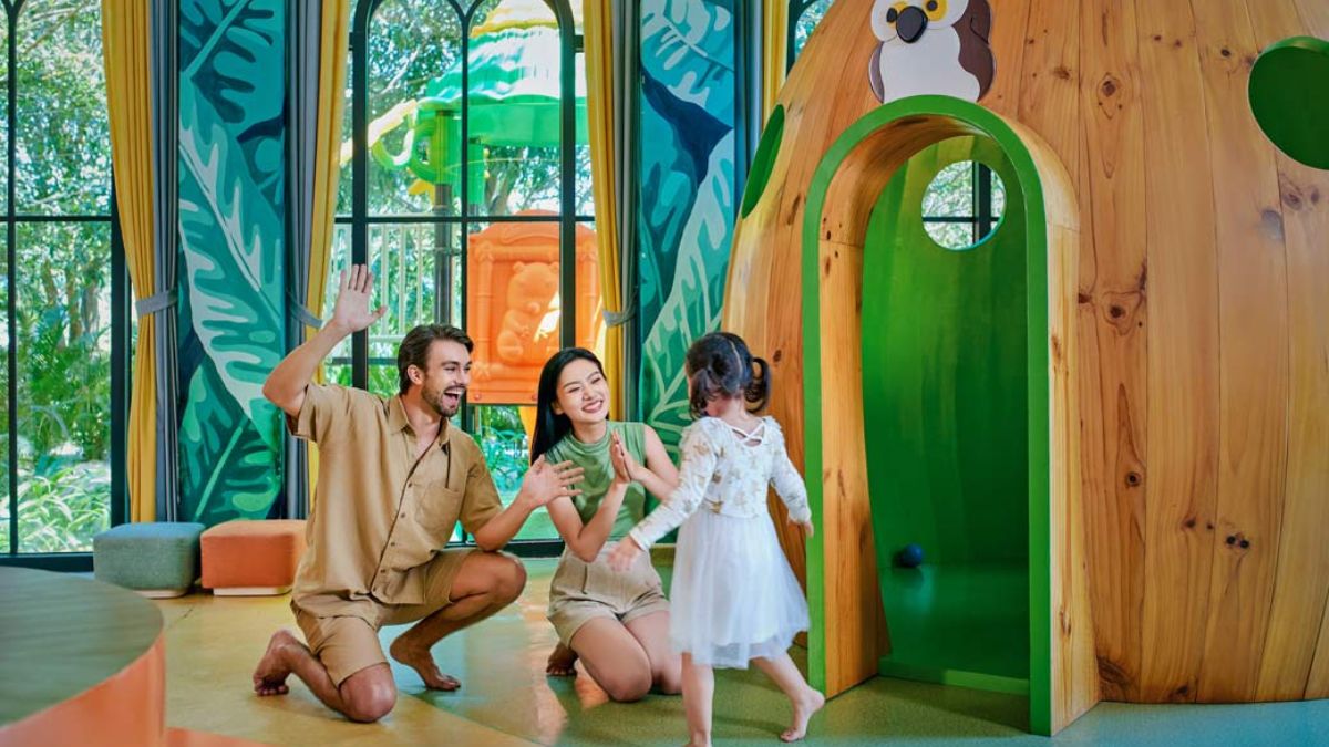 A family with a young child enjoying playtime in a colorful indoor kids' club, featuring a wooden playhouse and nature-inspired décor.