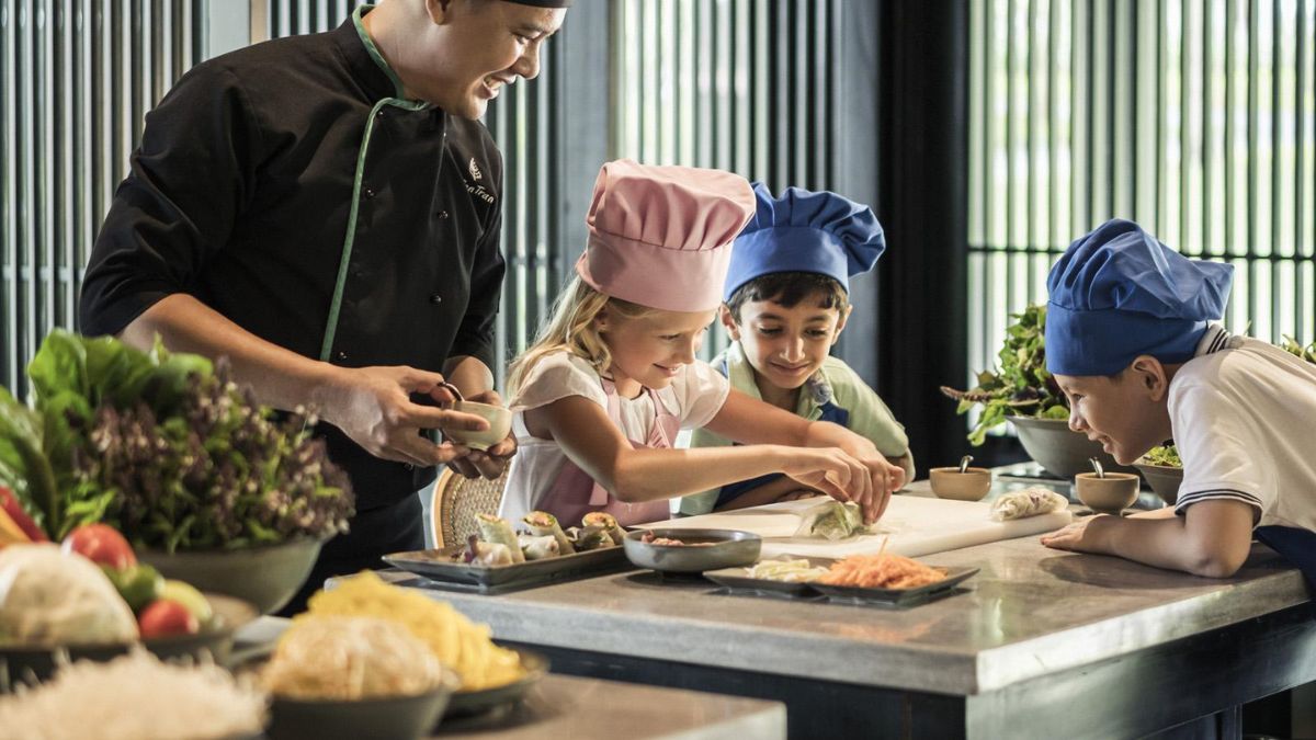 Foreign children wearing chef hats learn how to make fresh Vietnamese spring rolls during a hands-on cooking class with a local chef.