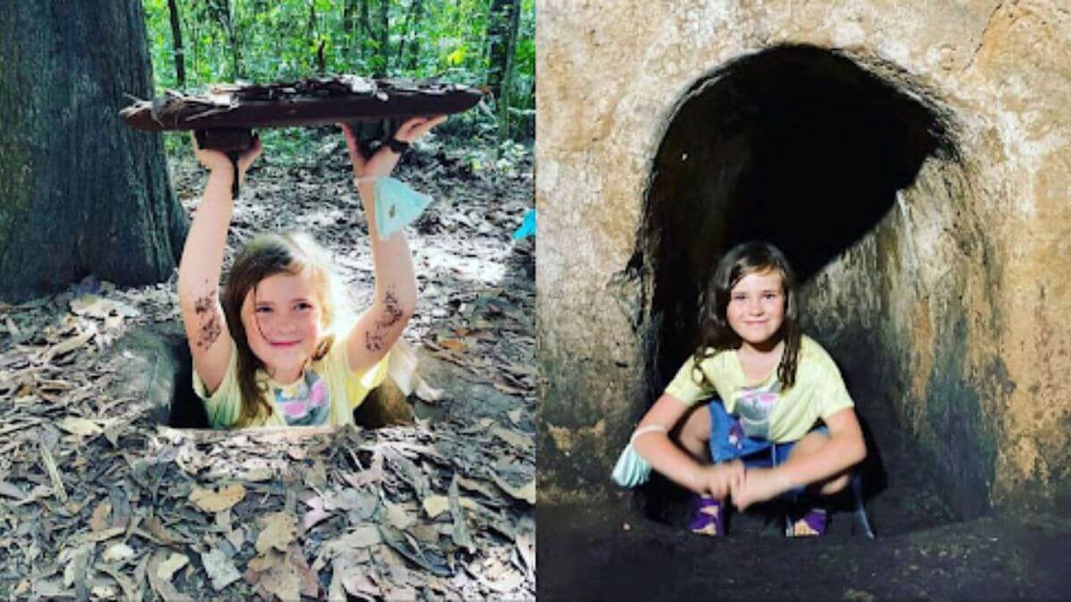 A young foreign girl explores the Cu Chi Tunnels near Ho Chi Minh City, emerging from a hidden tunnel entrance and sitting inside a narrow underground passage.