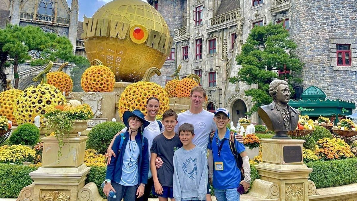 A foreign family with three children poses in front of the Sun World globe at French Village in Ba Na Hills, Da Nang, surrounded by European-style architecture and colorful flower displays.