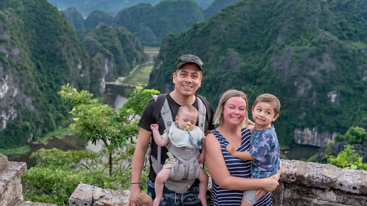 A foreign family with two young children posing at the Hang Mua viewpoint in Ninh Binh, Vietnam, overlooking dramatic limestone mountains and winding rivers.