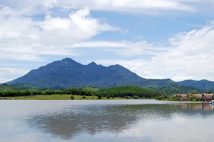 Mountain landscape reflected on a calm lake under a bright blue sky in Ba Vi, Vietnam.