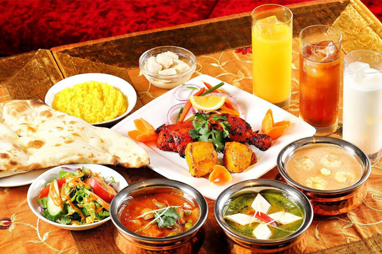 A traditional Indian meal featuring naan bread, curry dishes, grilled chicken, rice, salad, and refreshing drinks on a decorative table