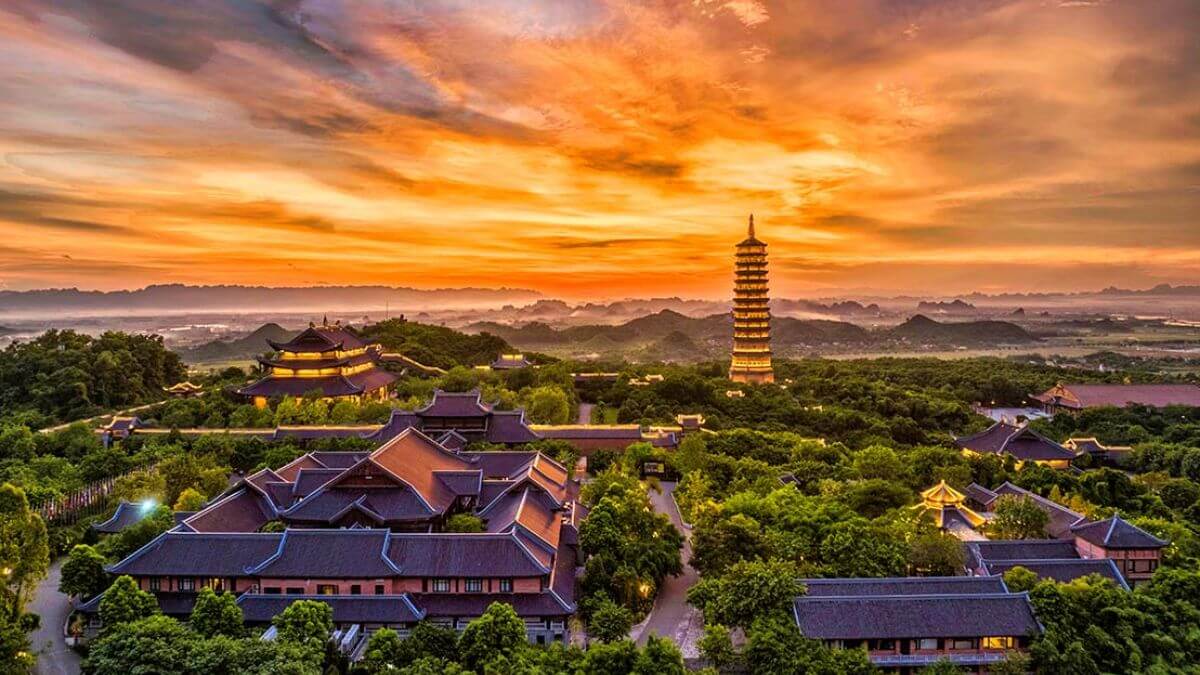 Panoramic sunset view of Bai Dinh Pagoda and its iconic Buddhist stupa surrounded by lush greenery in Ninh Binh, Vietnam.