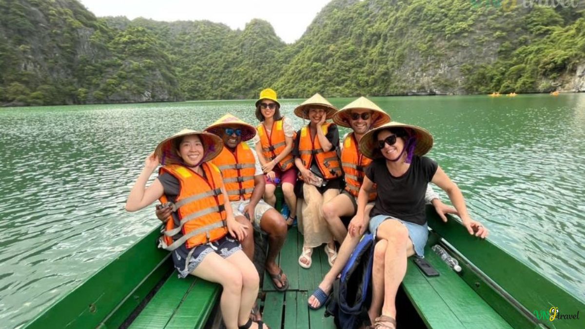 Tourists wearing traditional Vietnamese conical hats and life jackets on a boat tour through the emerald waters and limestone karsts of northern Vietnam.