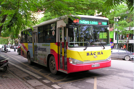 A public bus operating on a tree-lined street in Hanoi, Vietnam.