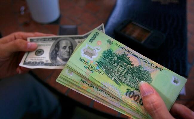 A traveler holding Vietnamese đồng and U.S. dollars during a currency exchange transaction in Vietnam, illustrating potential money exchange scams