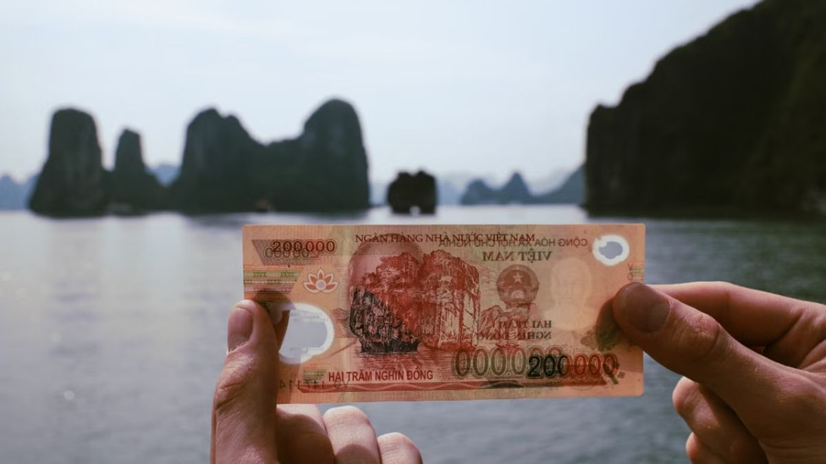 A traveler holds a Vietnamese 200,000 VND banknote in front of Ha Long Bay, highlighting the importance of understanding Vietnam’s currency and avoiding common money-related scams.