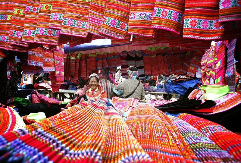 Colorful handmade textiles and local ethnic vendors at Dong Van Market in Ha Giang, Vietnam.