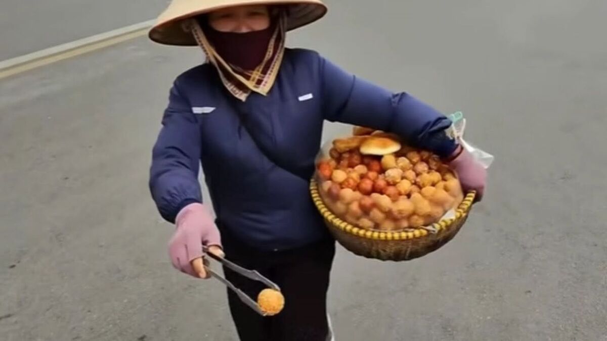A street vendor in Hanoi Old Quarter offers traditional Vietnamese donuts to passersby, highlighting the importance of confirming prices before purchasing from street vendors.