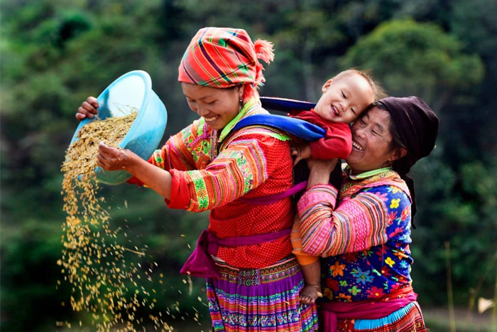 Women from an ethnic community in Cao Bằng wearing colorful traditional clothing while carrying a child outdoors.