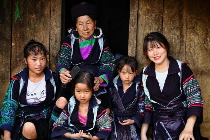 Ethnic minority family in traditional clothing posing in front of a wooden house in Sapa.