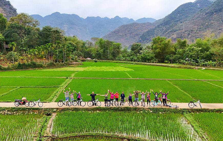 Travelers cycling through lush green rice fields in Mai Chau surrounded by mountains in northern Vietnam.