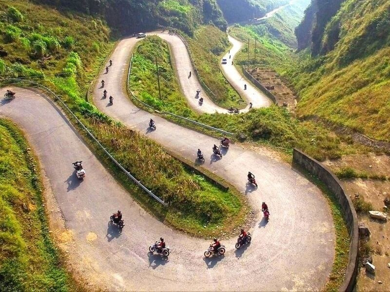 Motorbikes riding through the winding roads of the Ha Giang Loop surrounded by majestic mountains in northern Vietnam