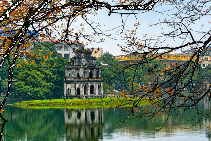 Turtle Tower reflected on Hoan Kiem Lake surrounded by trees in Hanoi, Vietnam.