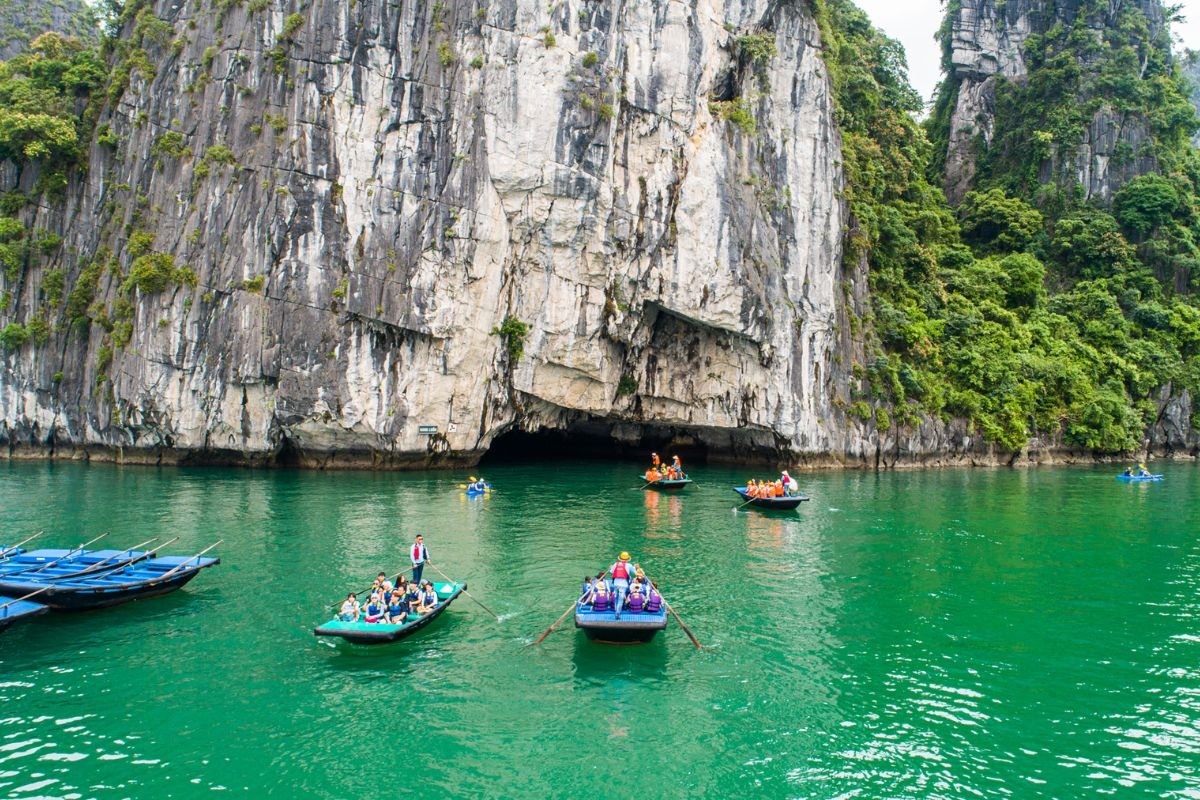 Tourists kayaking and boating through emerald waters beside limestone cliffs in Lan Ha Bay, Vietnam.