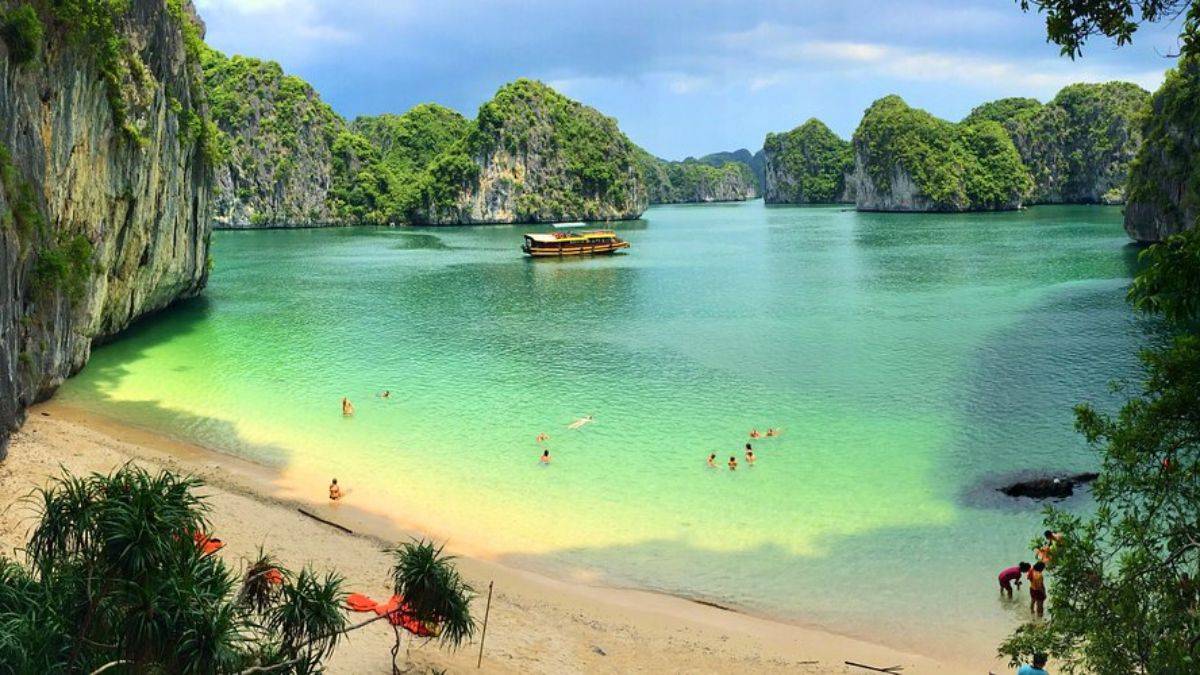 Lan Ha Bay with emerald waters, white sandy beach, limestone karsts, and visitors swimming in a peaceful tropical setting in northern Vietnam.