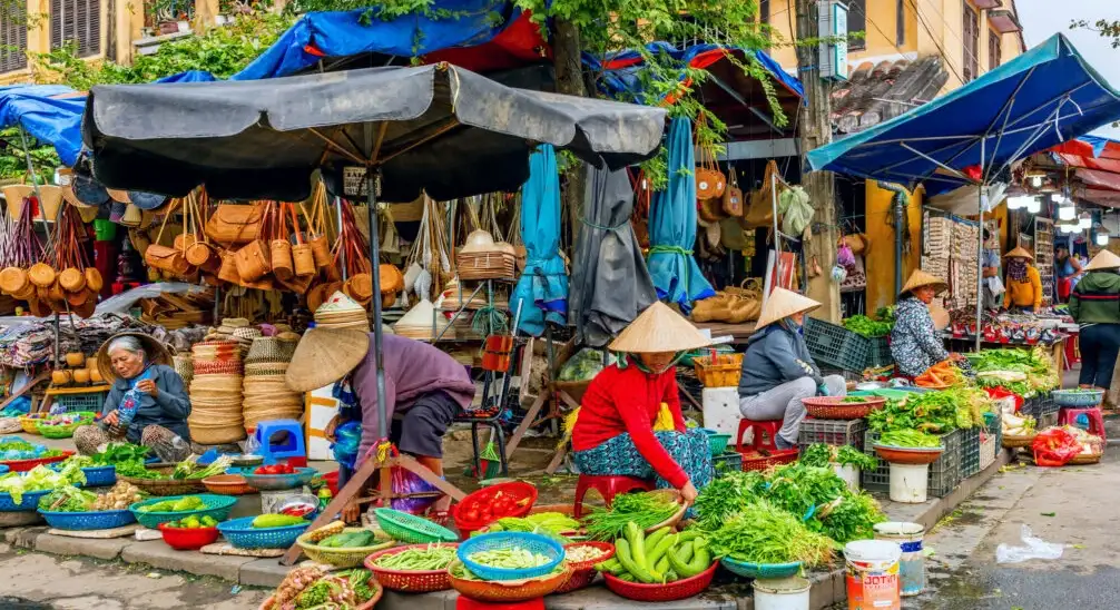 Local vendors selling fresh vegetables, fruits, and handmade goods at a traditional street market in Hoi An, Vietnam.