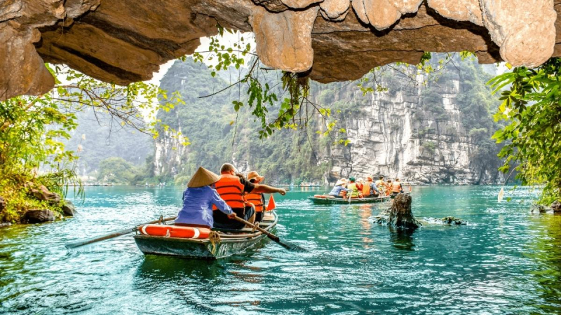 Tourists taking a boat ride through caves and emerald water in Ninh Binh, Vietnam.
