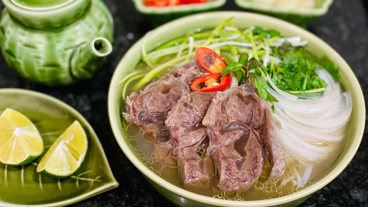 Traditional Vietnamese beef pho served with tender sliced beef, rice noodles, fresh herbs, lime wedges, and chili peppers in a flavorful broth.