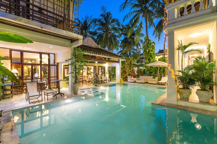 Luxury resort in Da Nang with a swimming pool, tropical palm trees, and elegant villas illuminated at night.