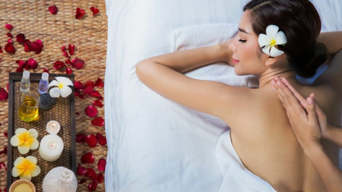 Woman enjoying a relaxing massage treatment at a luxury spa with aromatic oils, candles, and tropical flowers.