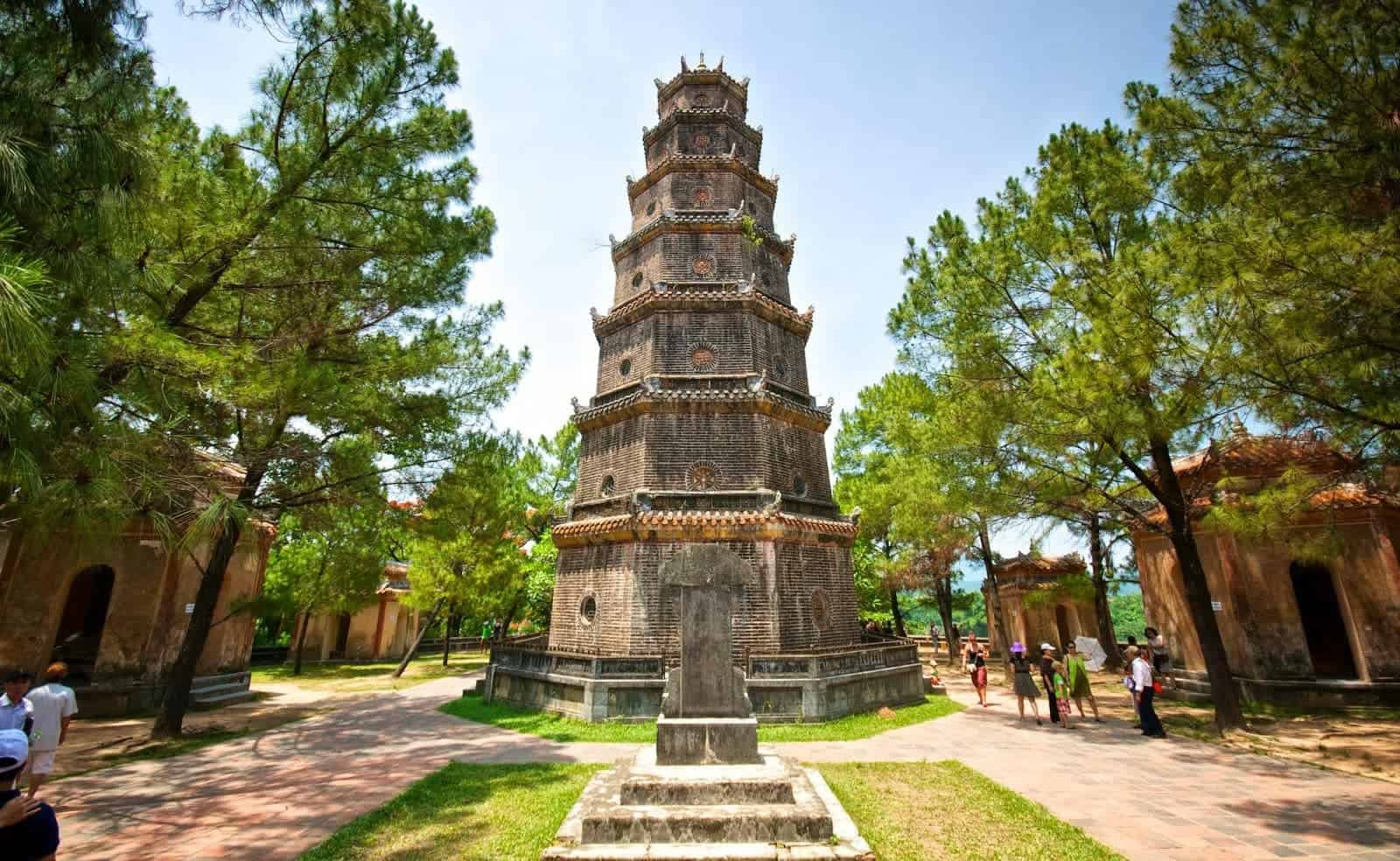 Thien Mu Pagoda in Hue featuring the iconic seven-story Phuoc Duyen Tower surrounded by lush green pine trees and historic temple grounds.