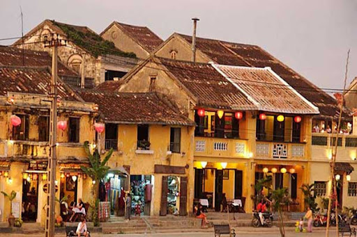Traditional yellow houses with tiled roofs and glowing lanterns along the riverside in Hoi An Ancient Town, Vietnam.