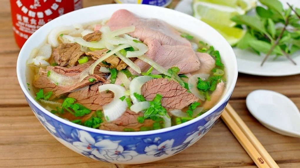 Close-up bowl of traditional Hanoi pho with beef, rice noodles, fresh herbs, and clear broth in Vietnam.