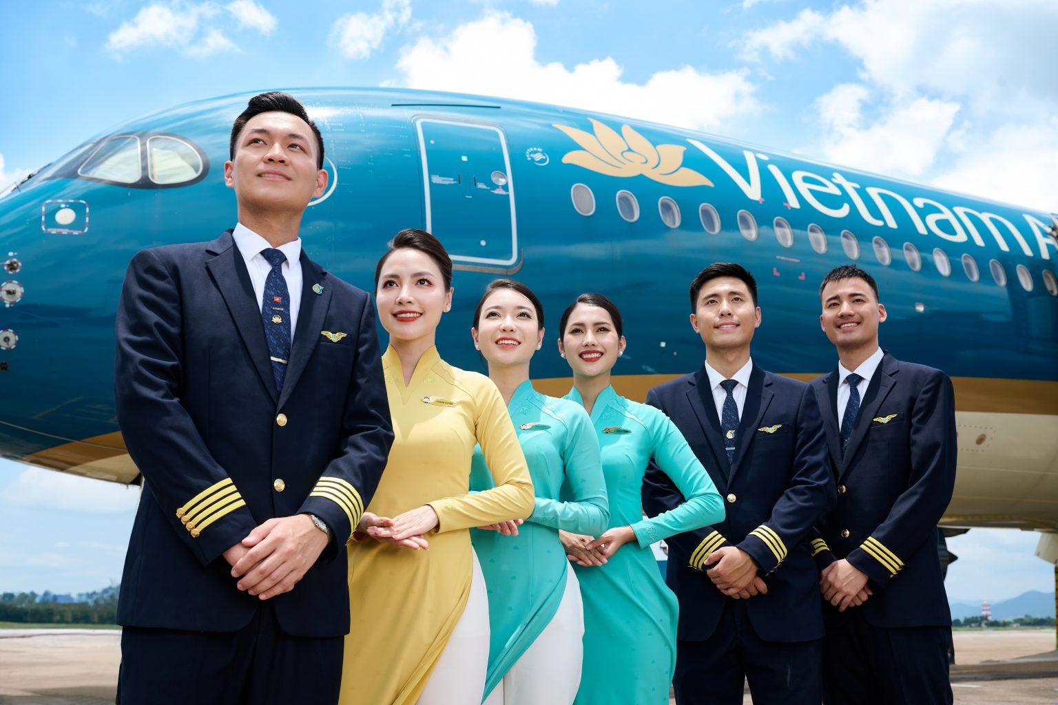 Vietnam Airlines pilots and flight attendants standing in front of a Vietnam Airlines aircraft at the airport.