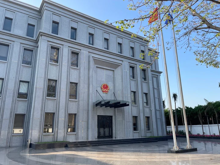 Exterior view of a modern government building in Vietnam with the national emblem above the entrance and flags displayed outside