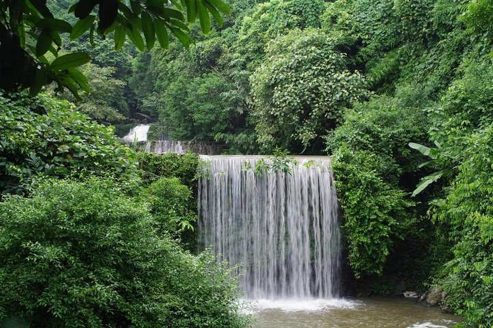 Small waterfall flowing through dense green tropical forest in Ba Vi National Park, Vietnam.